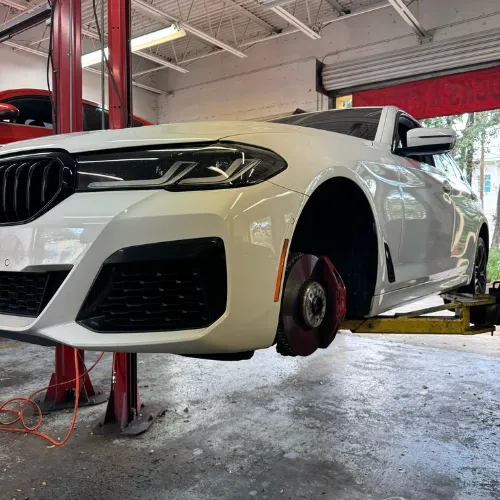 White BMW on a lift at AutoPlus with the wheel removed for brake repair
