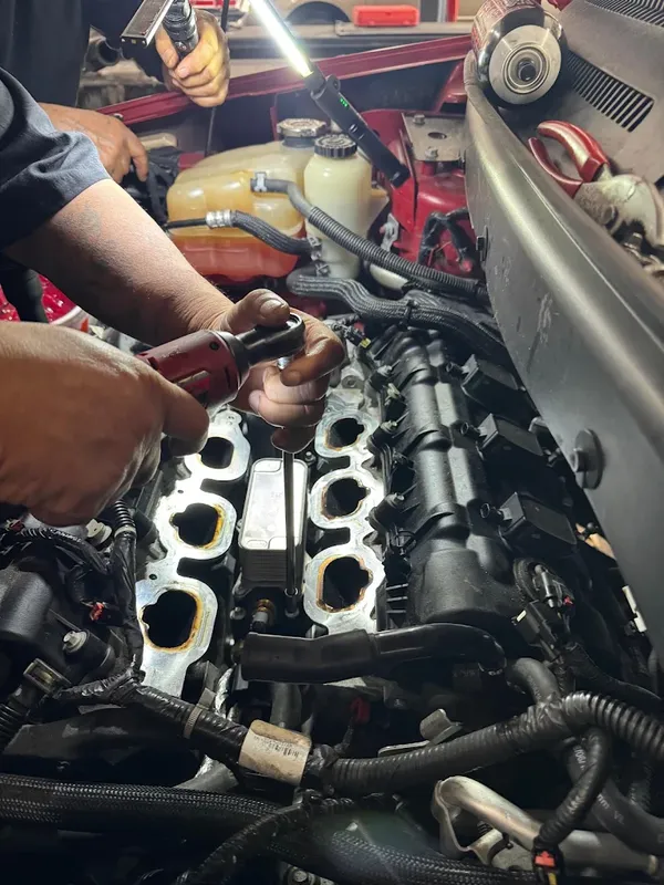 AutoPlus technician working in an engine bay with the intake manifold removed