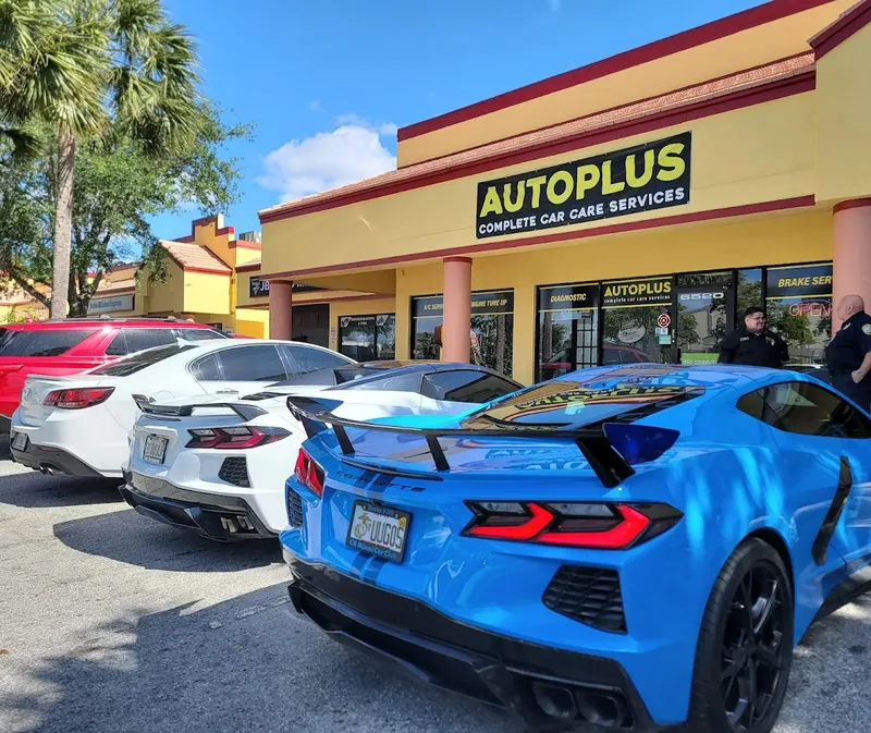 AutoPlus storefront with customer vehicles including a blue Corvette parked out front